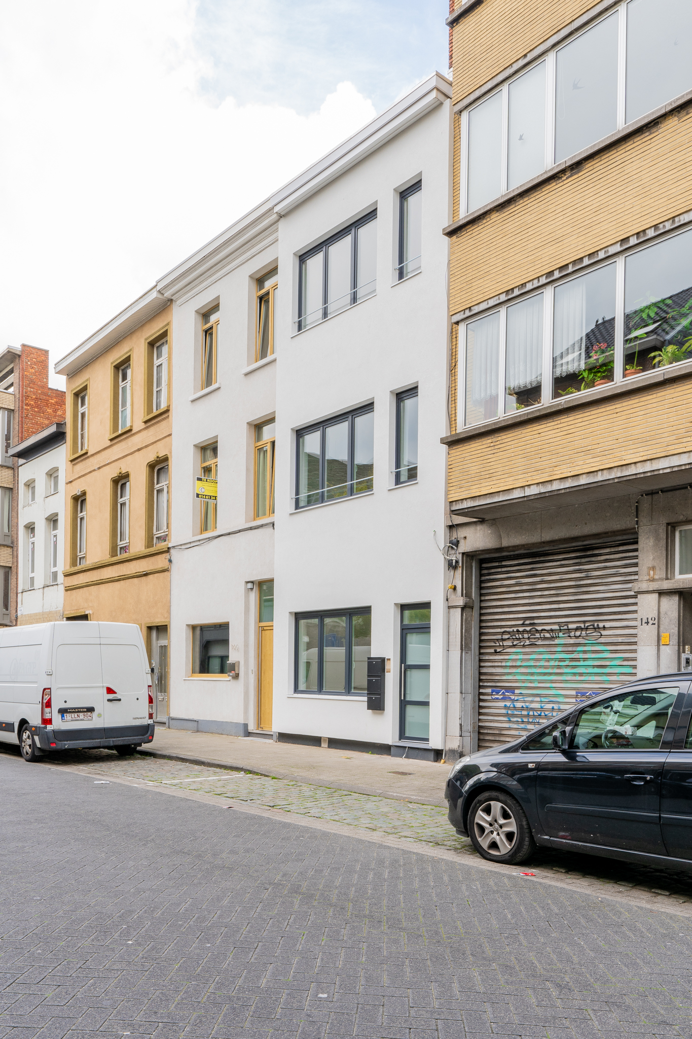 Vernieuwde witgepleisterde gevel van een Antwerpse stadswoning met donkere raamprofielen